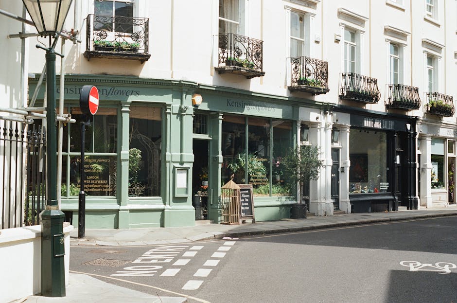 A charming florist storefront with a pale green facade, featuring large glass display windows showcasing fresh floral arrangements. The shop, part of dalstonflowers.org.uk, is located on Kingsland Roa