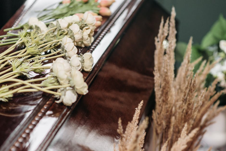 A floral arrangement featuring a bouquet of white roses, some with hints of peach, resting along the edge of a polished wooden surface, possibly a piano or table, with visible stems and fresh petals.